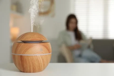 Essential oil diffuser on table, space for text. Woman reading book in room.. Stock Photos