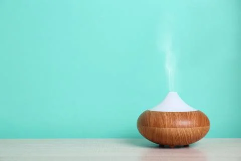 Essential oils diffuser on table near turquoise wall. Space for text Stock Photos