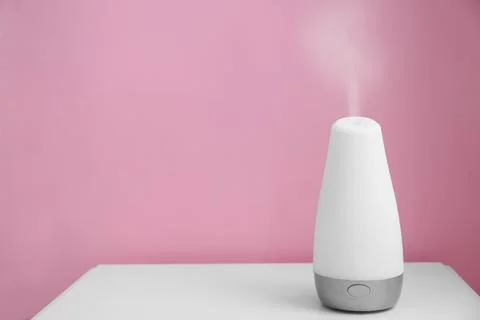 Essential oils diffuser on white table   near pink wall. Space for text Stock Photos