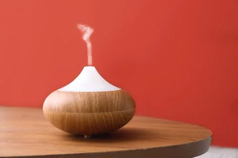 Essential oils diffuser on wooden table near red wall. Space for text Stock Photos