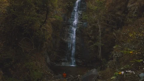 Establishing shot of man sitting in front of beautiful waterfall Stock Footage 87612193