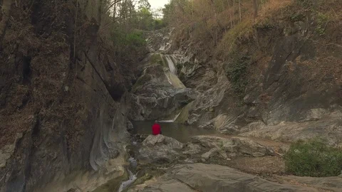 Establishing shot of man sitting in front of beautiful waterfall Stock Footage 87613812