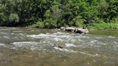 Establishing shot. small river rapids and fisherman in the distance. Vidéo 77481672