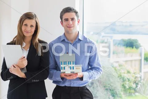 Estate agent holding clipboard and man holding miniature model house Stock-Fotos