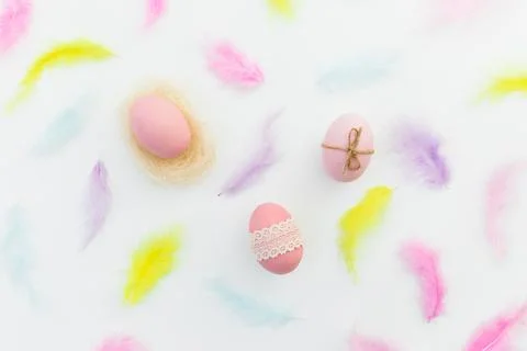 Ester composition with colorful eggs and pastel feathers on white background. Stock Photos