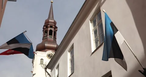 Estonian flags flutter beneath Tallinn church clock tower Stock Footage 320168643