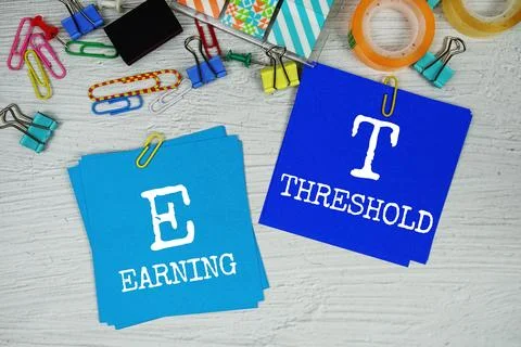 ET - Earning Threshold text on stick note with stationery on concrete backg.. Stock Photos
