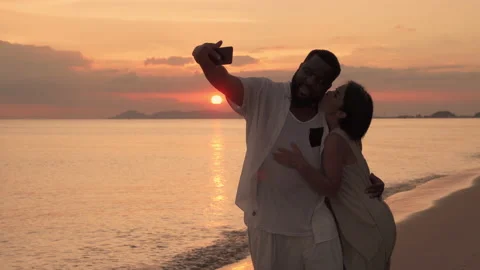 Ethnic couples taking selfies in the setting sun on the beach at sunset Stock Footage 143152596