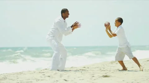 Ethnic father and son playing together American football on beach Stock Footage