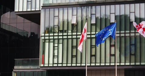 The EU and Georgian flags flutter against the background of the glass facade of Video stock 275529111