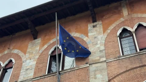 EU flag waving on historic brick building with arched windows in Pisa Stock Footage 306959843