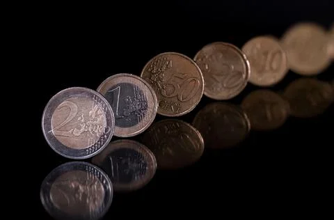 Euro coins standing on the edge isolated with pitch black background, reflecting Stock Photos