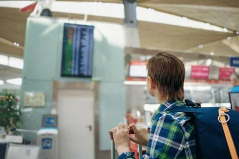 European boy in cap with backpack checking flight time at departure board i.. Stock-Fotos