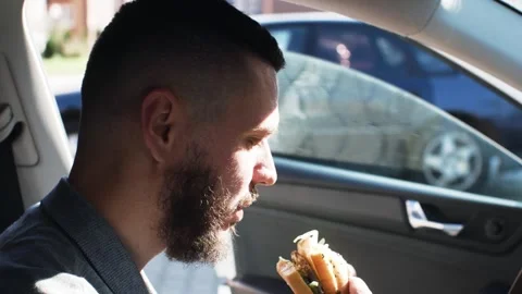 A European eats in the car. A hamburger snack. There is a working person in  Stock Footage 297776280