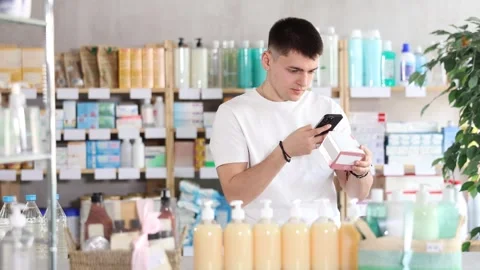 European guy in summer clothes is standing in a pharmacy and scanning the Stock Footage 344774331