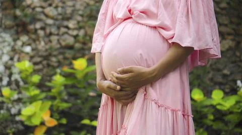 European pregnant girl in a pink dress gently touches her big stomach with he Stock Photos