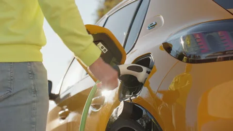 EV Car or Yellow Electric car charging station man's hand pulls out power cable Stock Footage 238546202