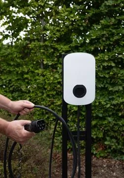 EV Close-up of hands connecting cables to an electric vehicle charger Stock Photos