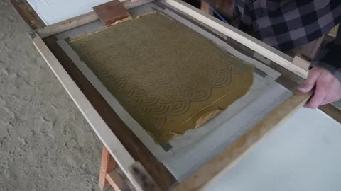 Even coat of khaki resist paste covers the wave stencil as the dyer smooths the Stock Footage 342902766