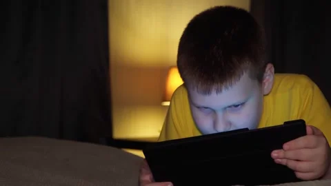 In the evening, a 10-year-old boy plays on a digital tablet in the bedroom. Stock Footage 263466599