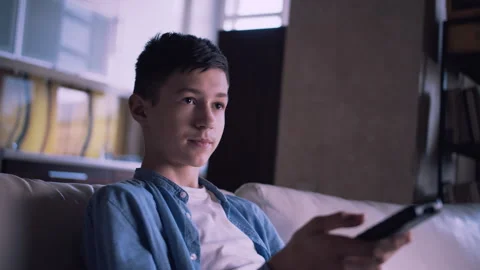 Evening Chill: Young Boy Browsing TV Channels from the Comfort of the Couch 스톡 동영상 317765570