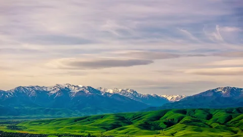 Evening clouds flying above snowcapped mountain range with green foothills Stock Footage 289532384