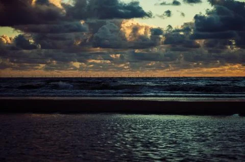Evening clouds lit by sunset over a sea with an offshore windmill park on the ho Stock Photos