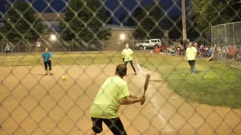 Evening coed softball batter get hit Run scores Viewed through back stop-SloMo Stock Footage 77845761