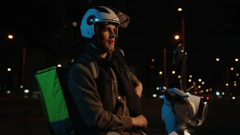 Evening delivery to the client.Man parks the scooter, looks at the right address Stock Footage 233984077