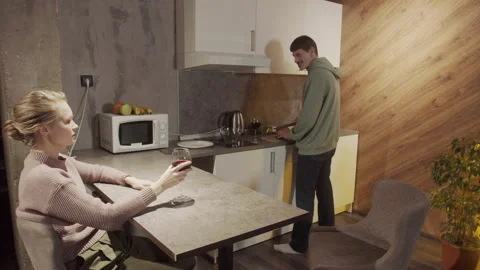 In the evening, the guy cuts fruit in the kitchen, the girl sits at the table Stock Footage 145071216