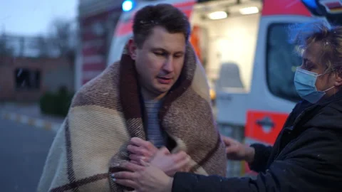 In the evening, it snows and the paramedic wraps the man in a blanket before Stock Footage 254197527