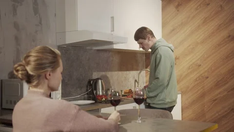 In the evening, in the kitchen, a man cuts vegetables for a salad, while his Video stock 145083855