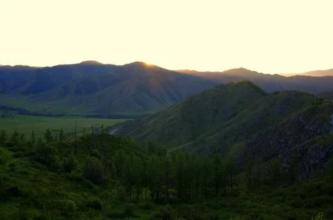 The evening landscape, the setting sun hid behind high mountains, illuminatin Stock Photos