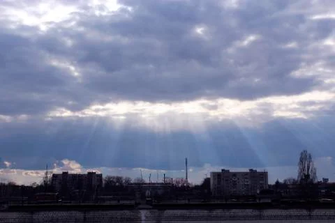 Evening landscape with sunny rays falling from clouds onto city Stock Photos