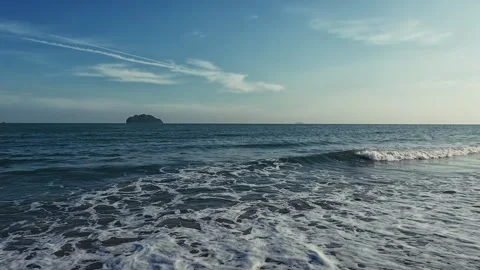 Evening ocean waves roll onto sandy shore as camera pans from shore silhouetted Video stock 332556662