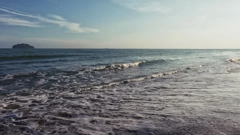 Evening ocean waves roll onto sandy shore as camera pans from sea to shore 動画素材 332556677