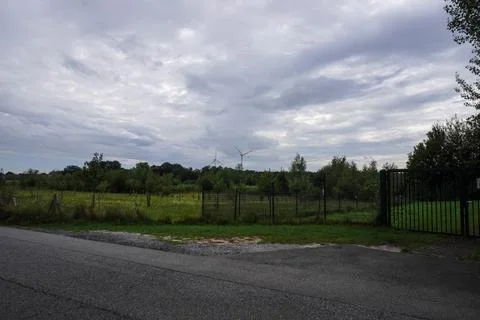 An evening park under a cloudy sky, with silhouettes of wind turbines visible Stock Photos