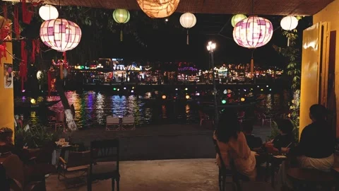 Evening relaxation at a riverside cafe with lanterns and lights Vídeo Stock 310428707