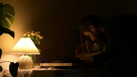 Evening scene with warm lamp light as a man bends over a vinyl record player 库存影片 330800656