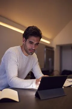 Evening Shot Of Man In Kitchen Working Or Studying From Home Using Digital Stock Photos