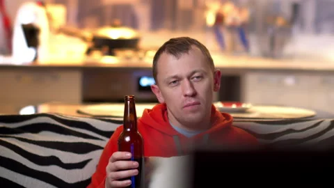 In the evening, sitting at the TV on the sofa, a young man drinks beer, camera Stock Footage 137175336