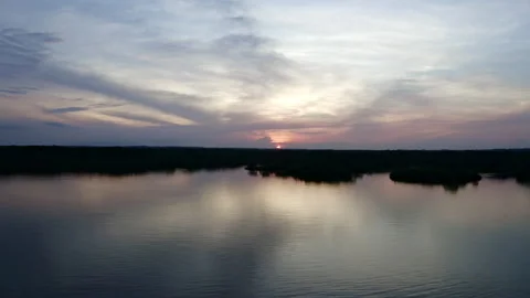 An evening sky during sunset over the silhouette of a forest next to a lake Stock Footage 169930208