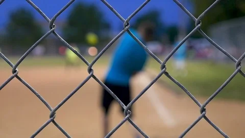Evening softball game through backstop Focus on wire Players out of focus Stock Footage 78114500