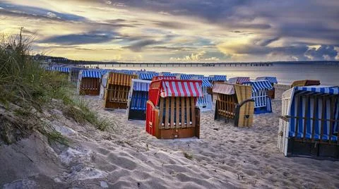 Evening sun with low light on beach filled with traditional wicker beach chai Stock Photos