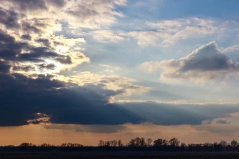 The evening sun sets behind dark clouds illuminating a land with its rays Stock Photos