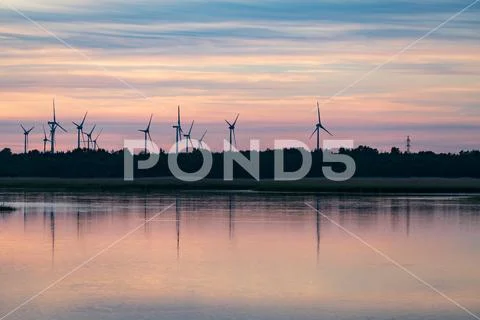 Evening sunlight on coast, pink and golden clouds and wind turbine. Sky refle Stock Photos