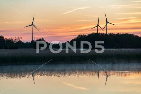 Evening sunlight on coast, pink and golden clouds and wind turbine. Sky refle Stock-Fotos