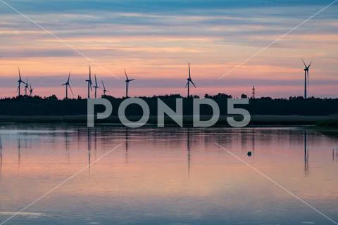 Evening sunlight on coast, pink and golden clouds and wind turbine. Sky refle Stock Photos