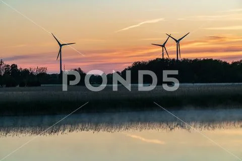 Evening sunlight on coast, pink and golden clouds and wind turbine. Sky refle Stock Photos