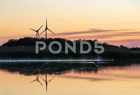 Evening sunlight on coast, pink and golden clouds and wind turbine. Sky refle Stock Photos